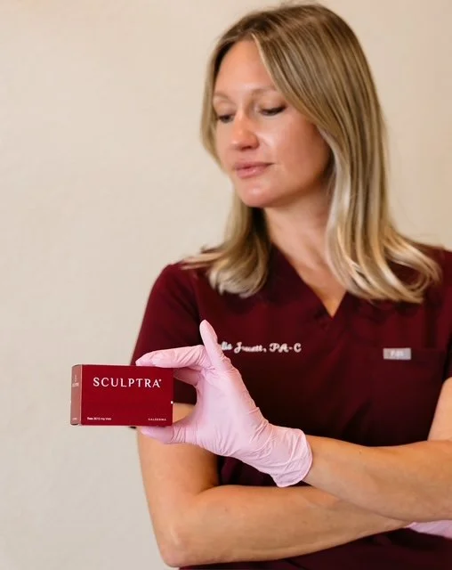 A woman in a maroon medical uniform holding a box of Sculptra, wearing pink gloves.