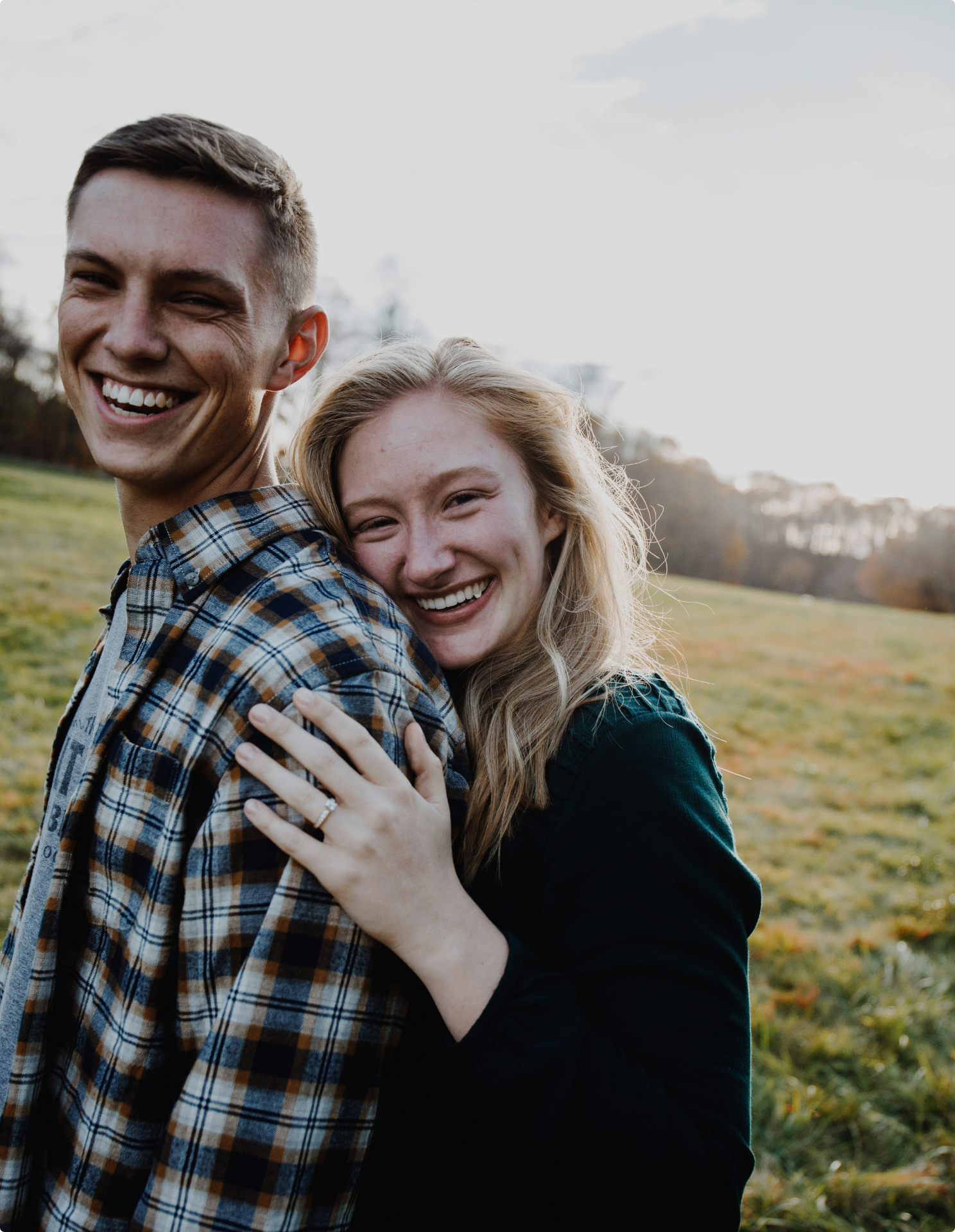 A young couple embracing outdoors in a field, smiling at the camera.