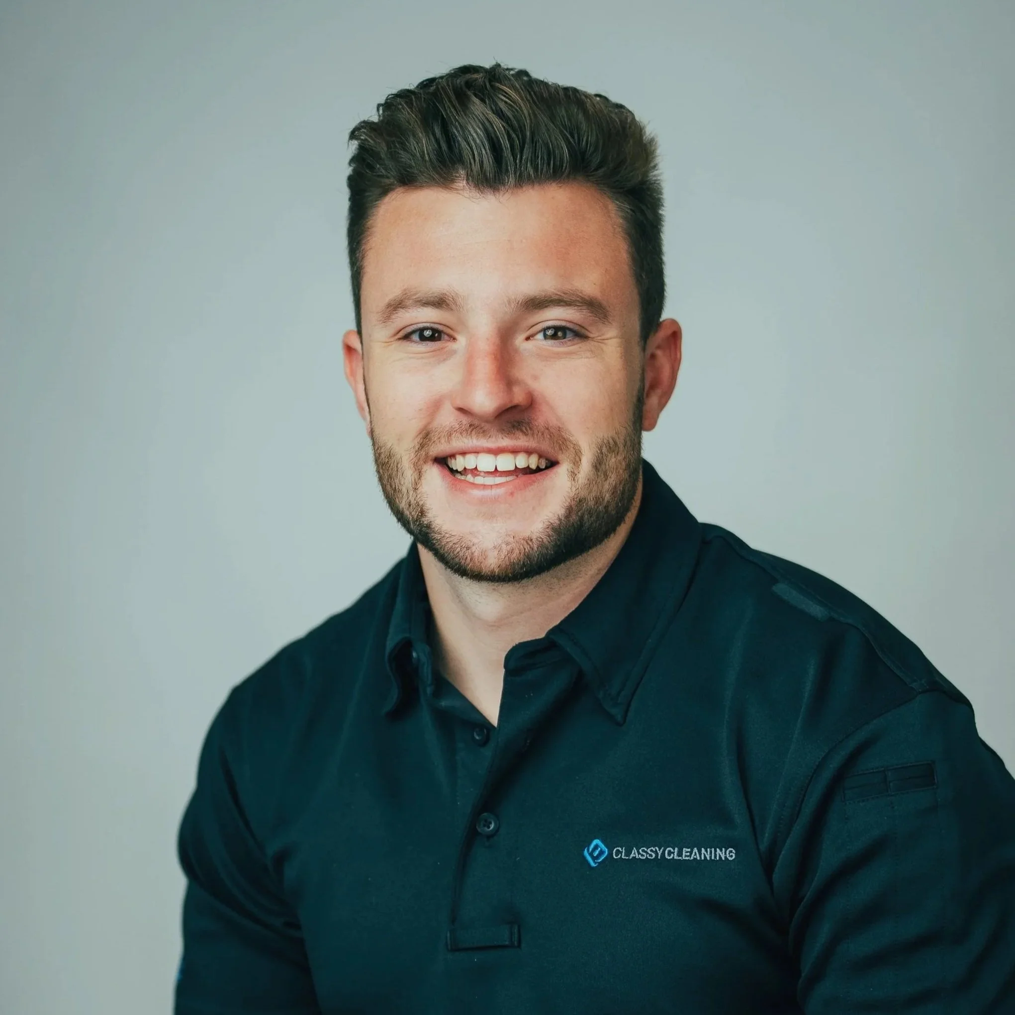 Headshot of a smiling man with dark hair and a beard wearing a black polo shirt with a logo that reads 'Classy Cleaning'.
