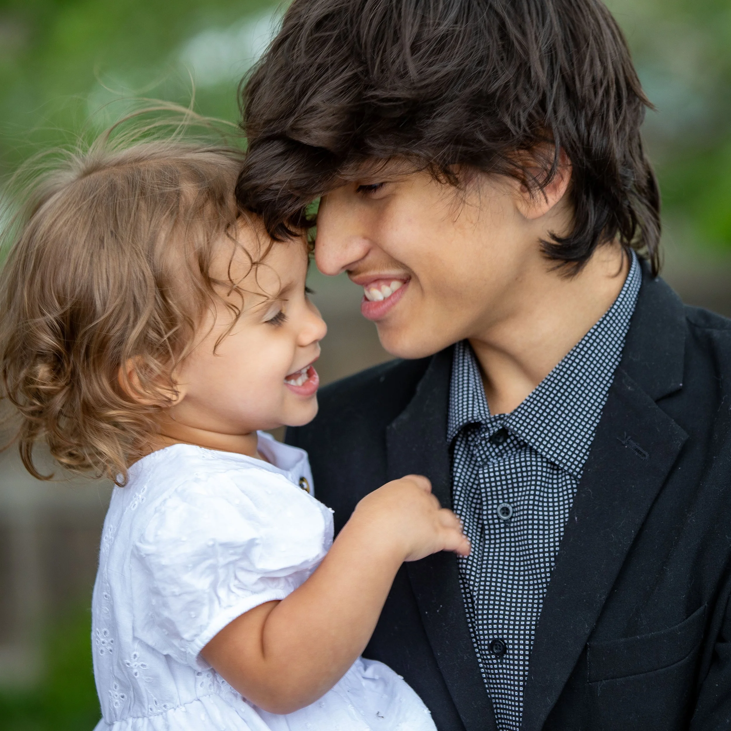 A young man and a little girl with their foreheads touching, smiling happily outdoors.  brother and sister editorial classic portrait photos