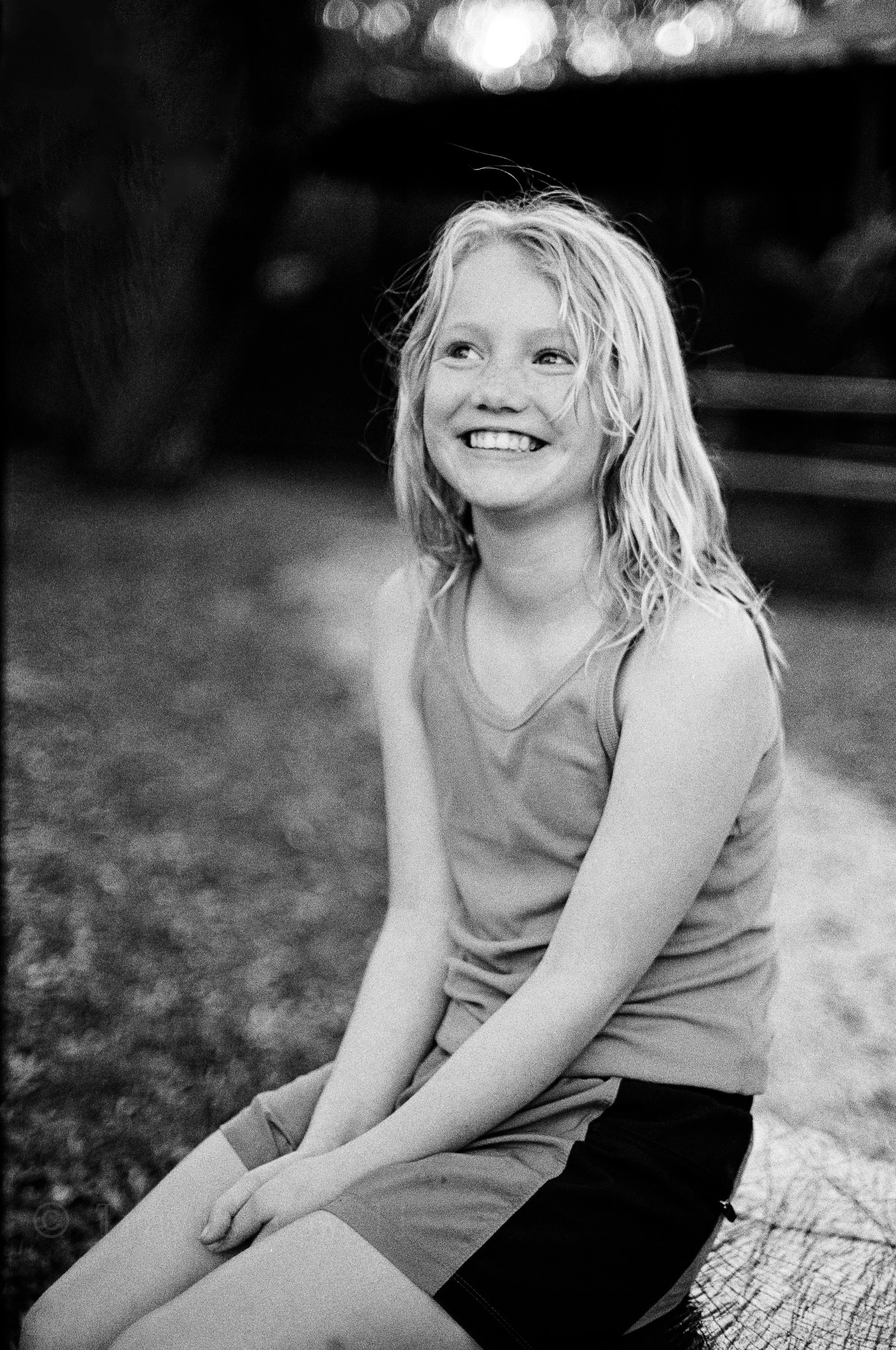 Outdoor portrait of a smiling girl with long wavy hair, photographed in a candid documentary style.