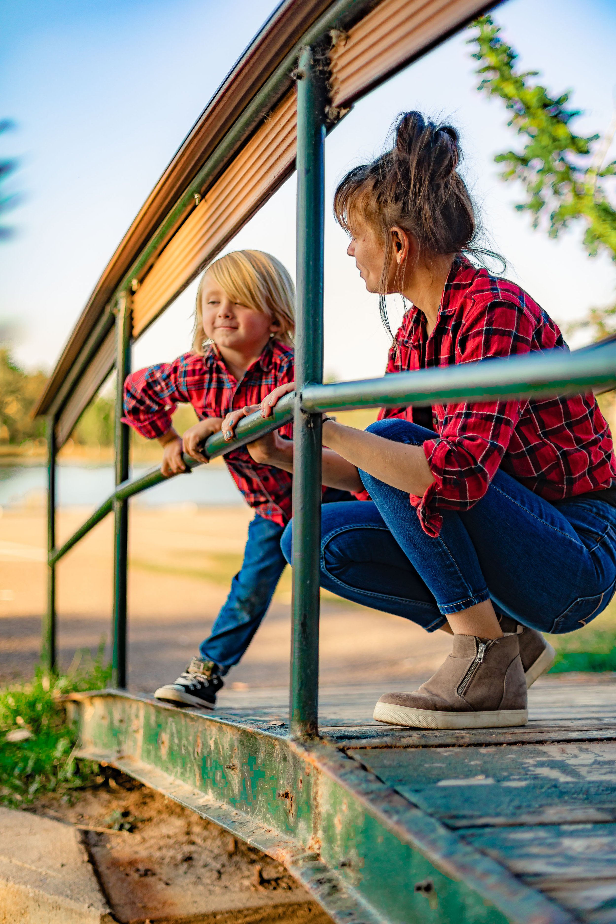 Mother and young son in matching red plaid shirts on a park playground structure.