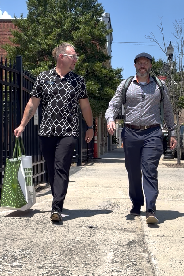 2 men walking down the street on the side walk.