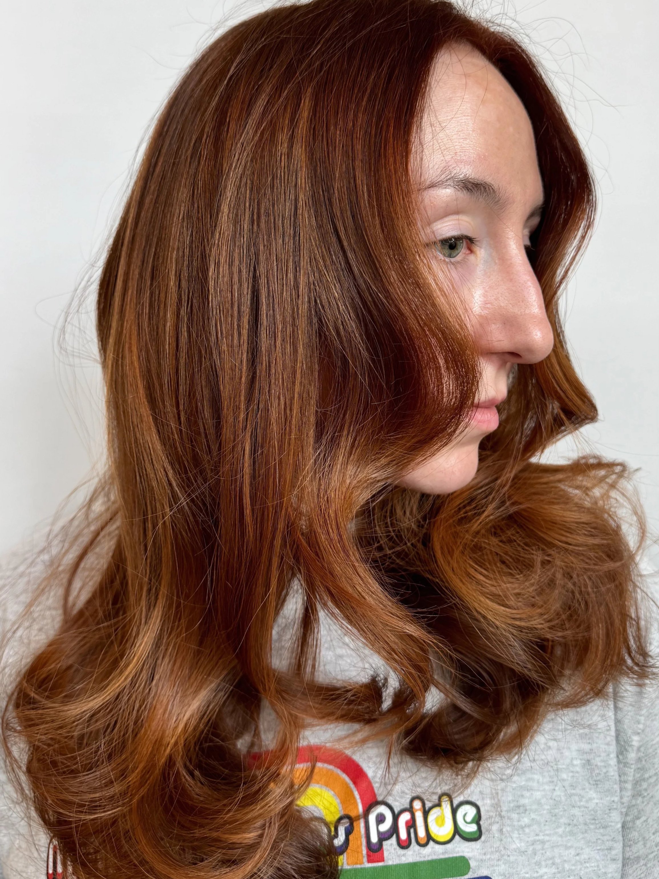 A side profile of a client displaying a vibrant, glossy auburn copper lived-in hair color and blowout at Little Saint Salon in Portland