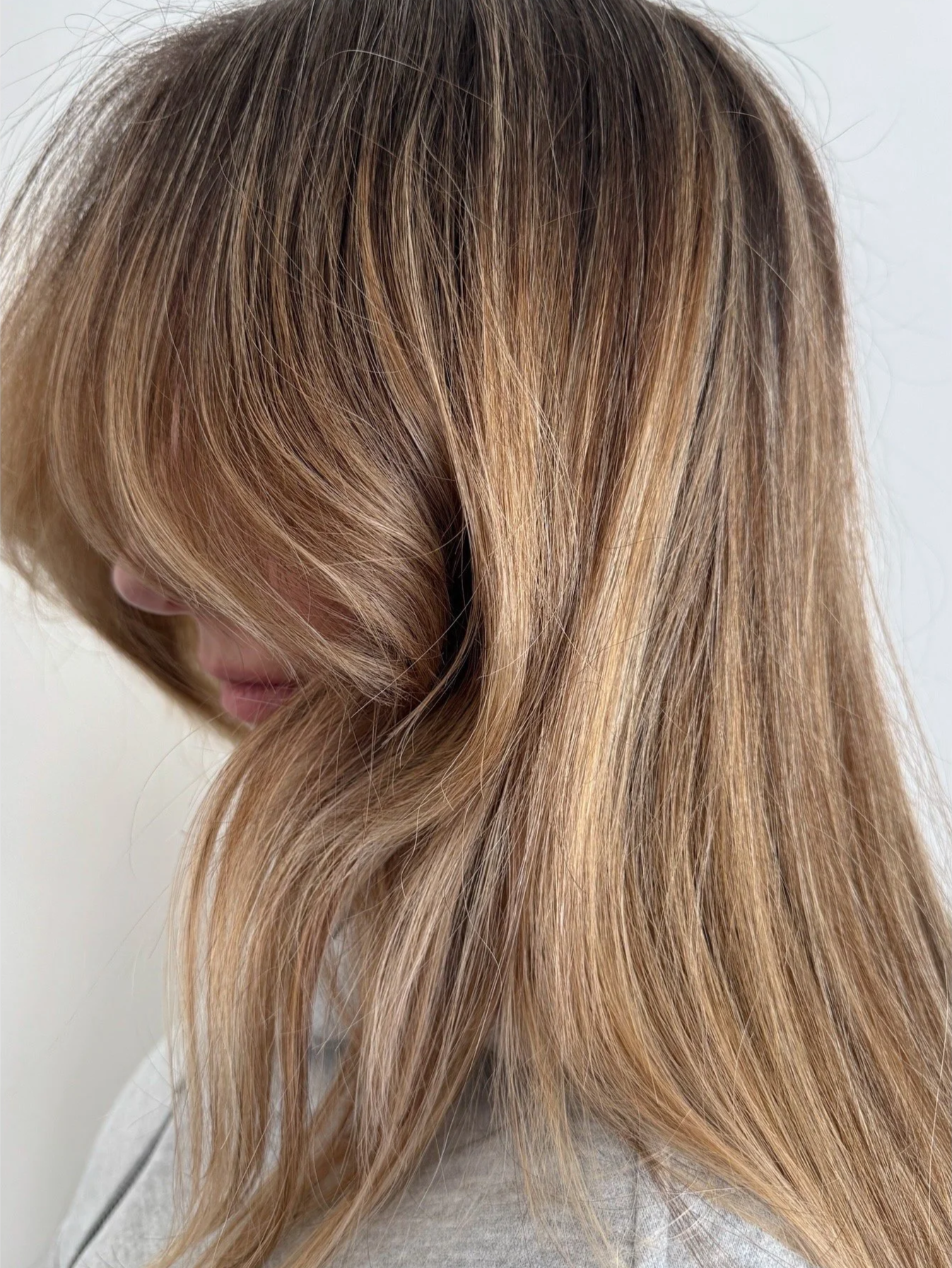A side profile of a client displaying a seamless golden blonde babylights color service paired with face-framing curtain bangs at Little Saint Salon in Portland