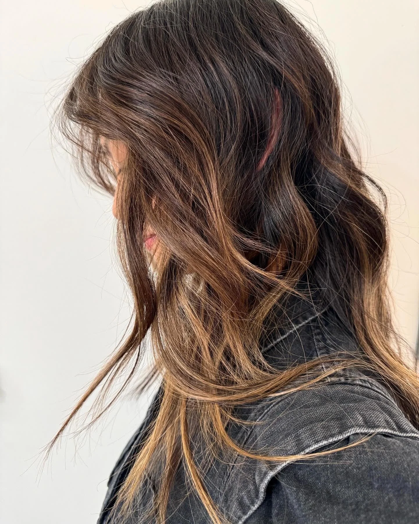 A side view of a client with long, wavy hair showcasing rich caramel brunette lived-in highlights at Little Saint Salon in the Kerns neighborhood