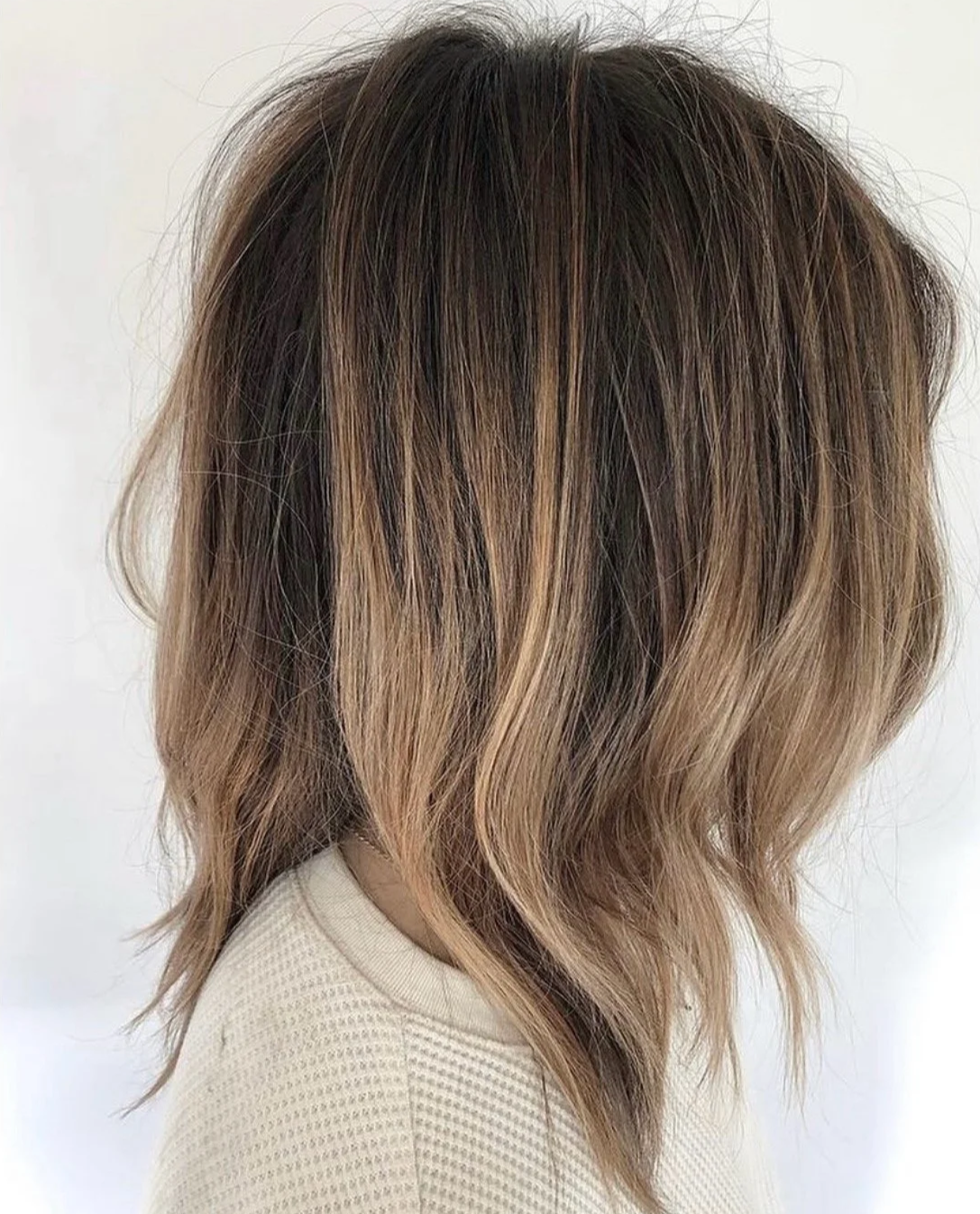 A brunette client with a textured mid-length cut showing bright, low-maintenance airtouch highlights from the blonde specialists at Little Saint Salon