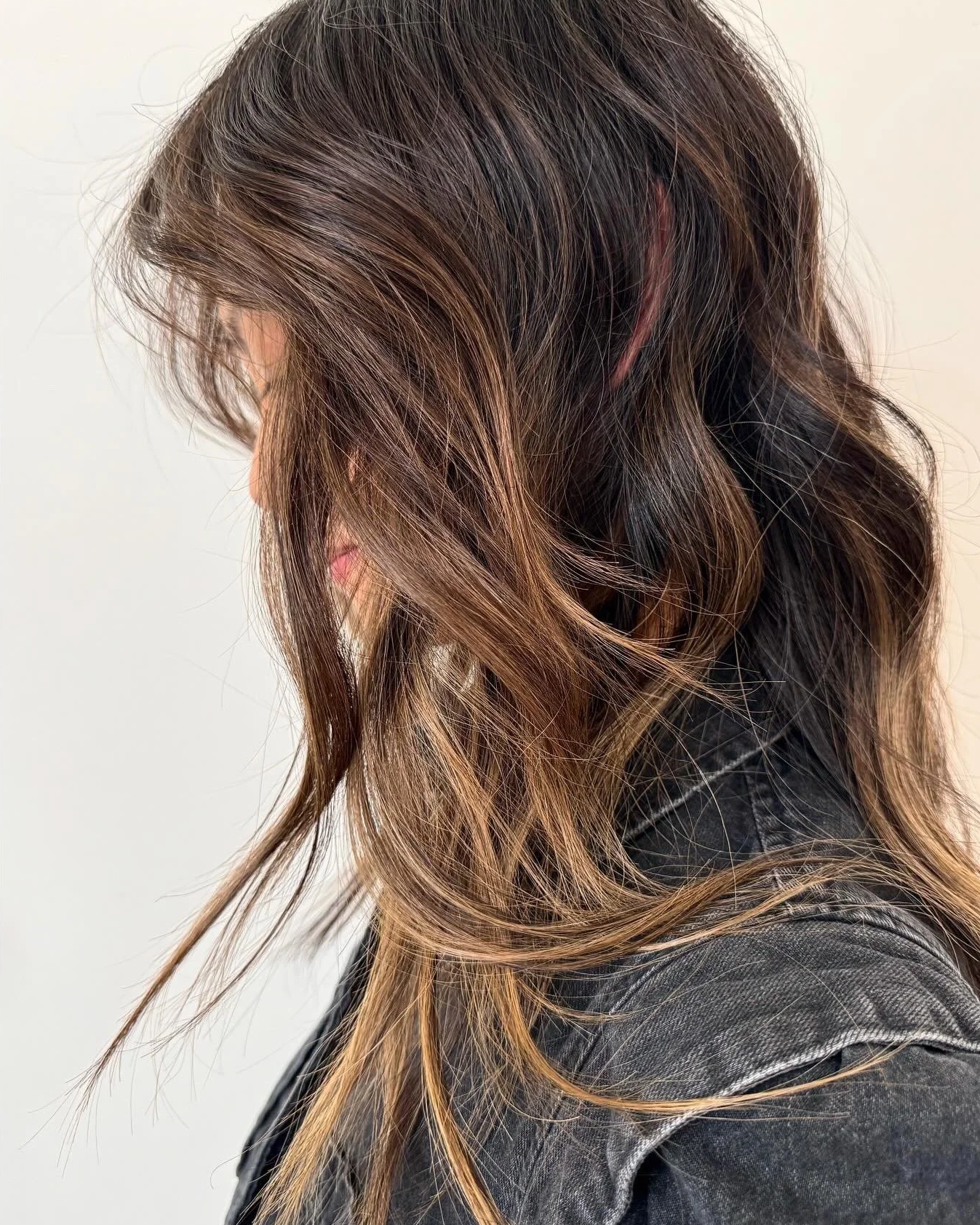 A brunette client with subtle sun-kissed blonde balayage ends and a textured style from the color specialists at Little Saint Salon
