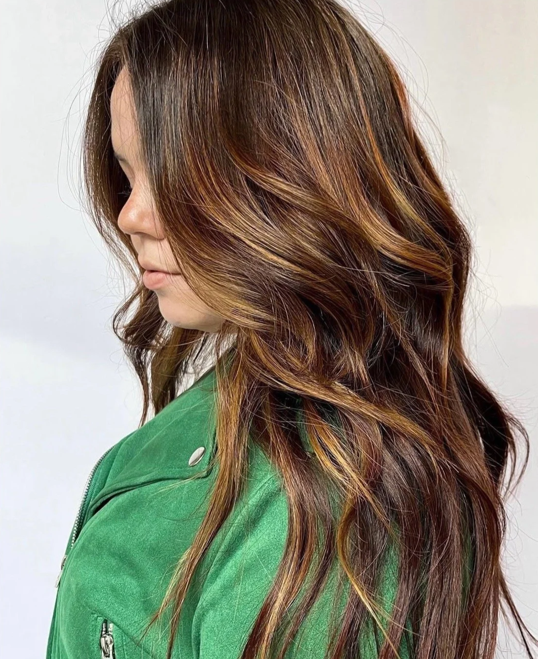A side view of a client with long, wavy hair showcasing rich caramel brunette lived-in highlights at Little Saint Salon in the Kerns neighborhood
