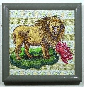 The art of Duyen Nguyen represented by Bywater Art Gallery of New Orleans during March- April 2026. Embroidery of a lion standing on green grass, with a red flower in its mouth, framed in a silver frame.
