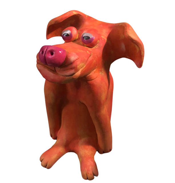 The art of Larone Hudson who is represented by Bywater Art Gallery of New Orleans Jan 2026. A sculpture of a pink and orange dog with large floppy ears, a pig-like snout, and googly eyes, made of clay or similar material.