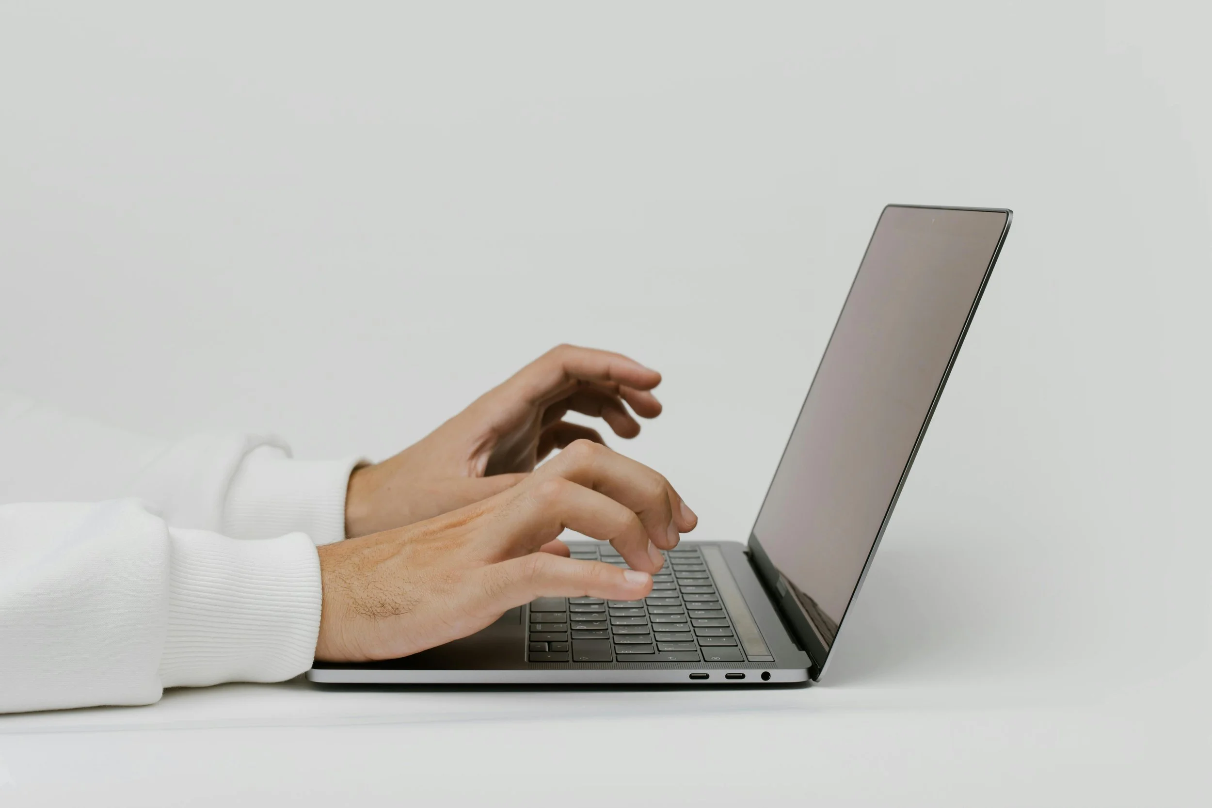 Hands typing on a laptop keyboard against a plain white background.