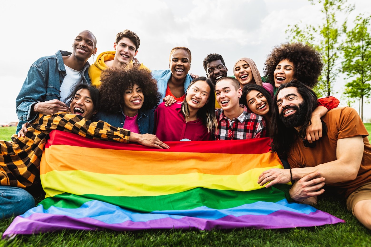 A diverse group of smiling people standing together behind a rainbow pride flag