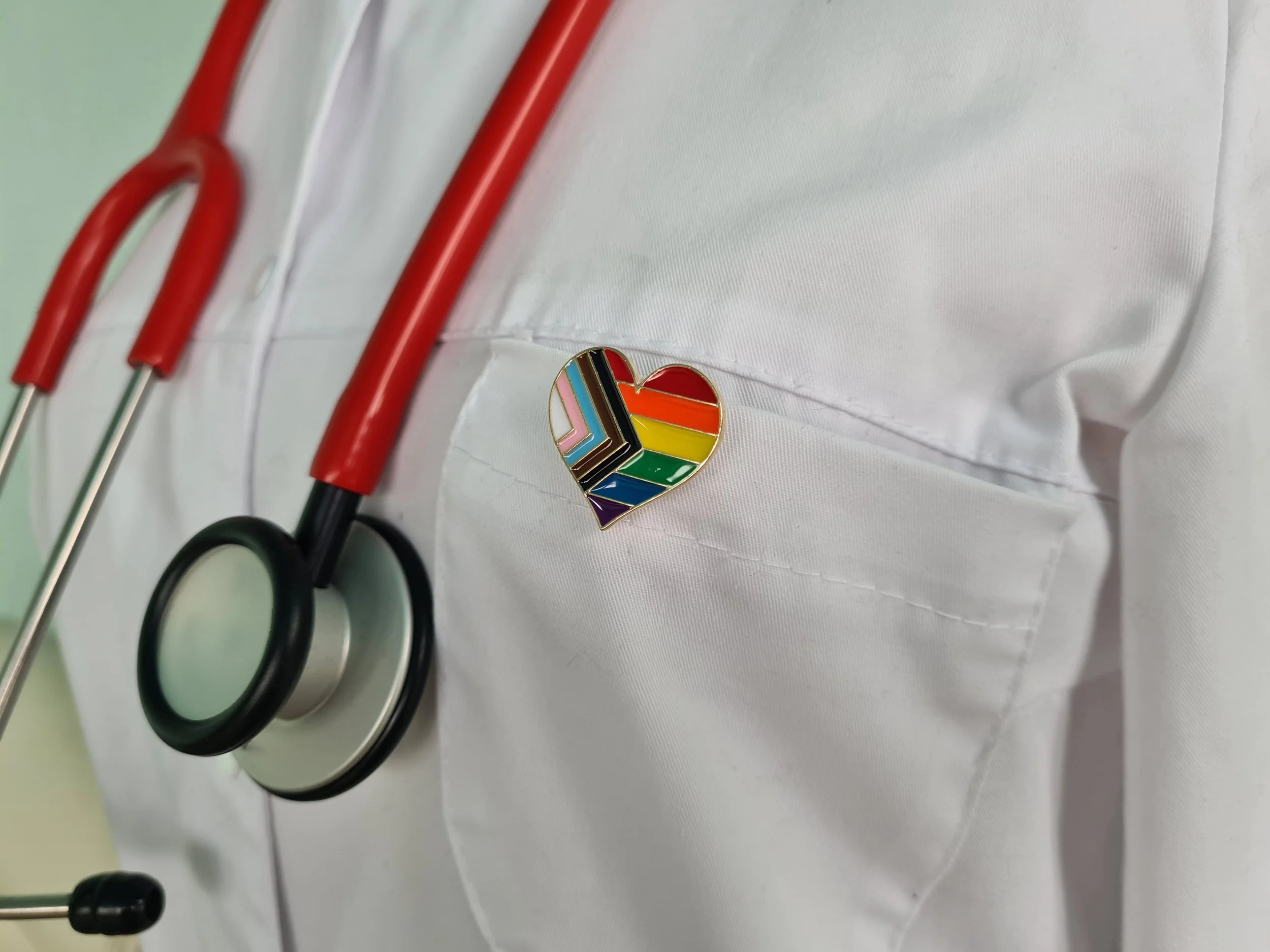 Doctor wearing a red stethoscope and pride progress pin shaped as a heart.