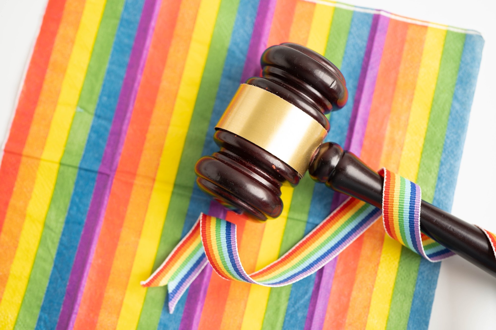 A wooden gavel resting on a rainbow Pride flag