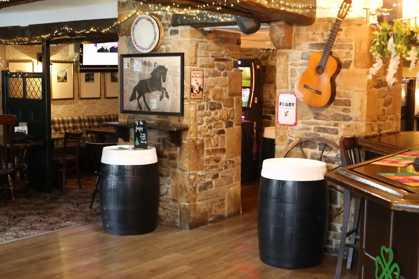 Interior of a rustic restaurant with stone walls, guitar on the wall, framed pictures, and tables with chairs.
