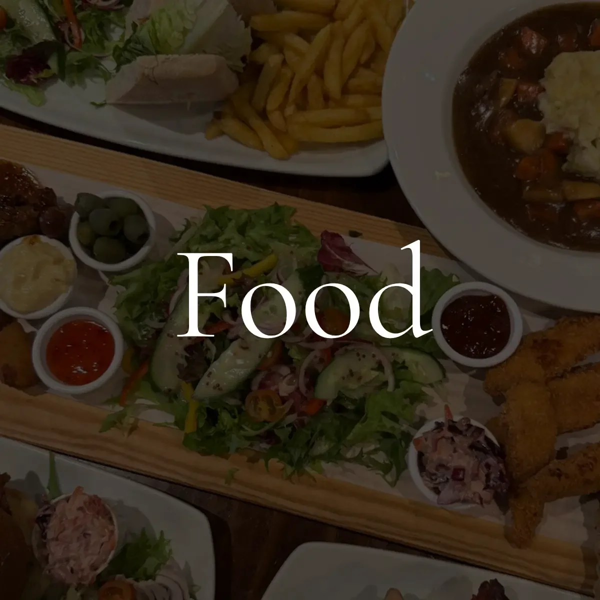 Assorted dishes including salad, French fries, fried chicken, breaded fish fillets, soup, and various sauces on plates and in bowls on a table.