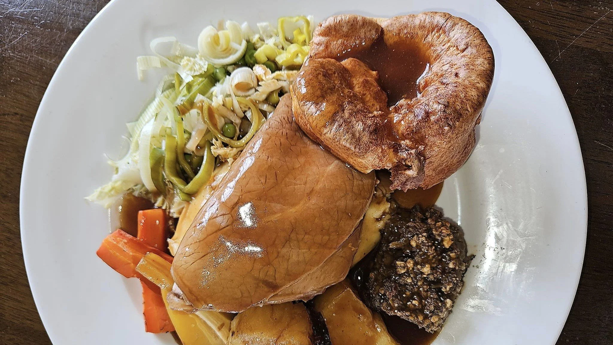 Plate of roast beef, Yorkshire pudding, mashed potatoes, carrots, peas, leek salad, and stuffing with gravy.