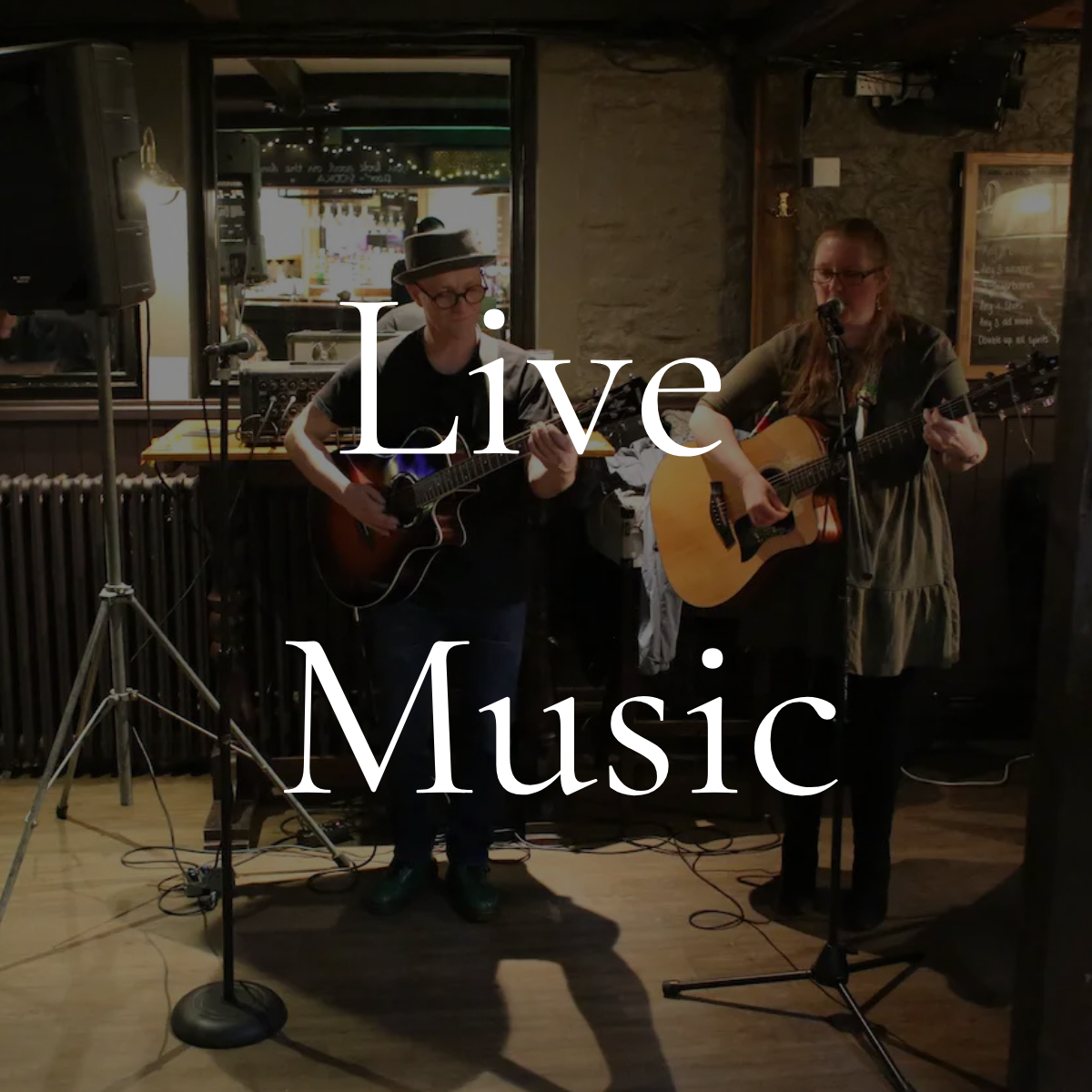 Two women playing acoustic guitars and singing at a live music performance in a cozy indoor venue.