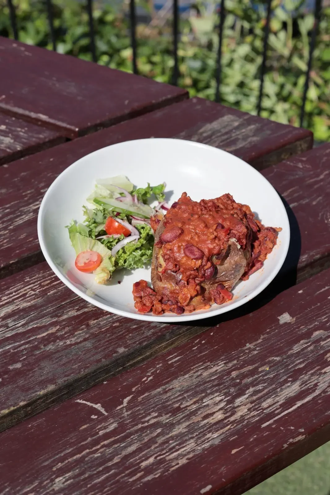 Plate with a large portion of baked stuffed eggplant topped with tomato sauce and a side of mixed greens salad with cherry tomatoes
