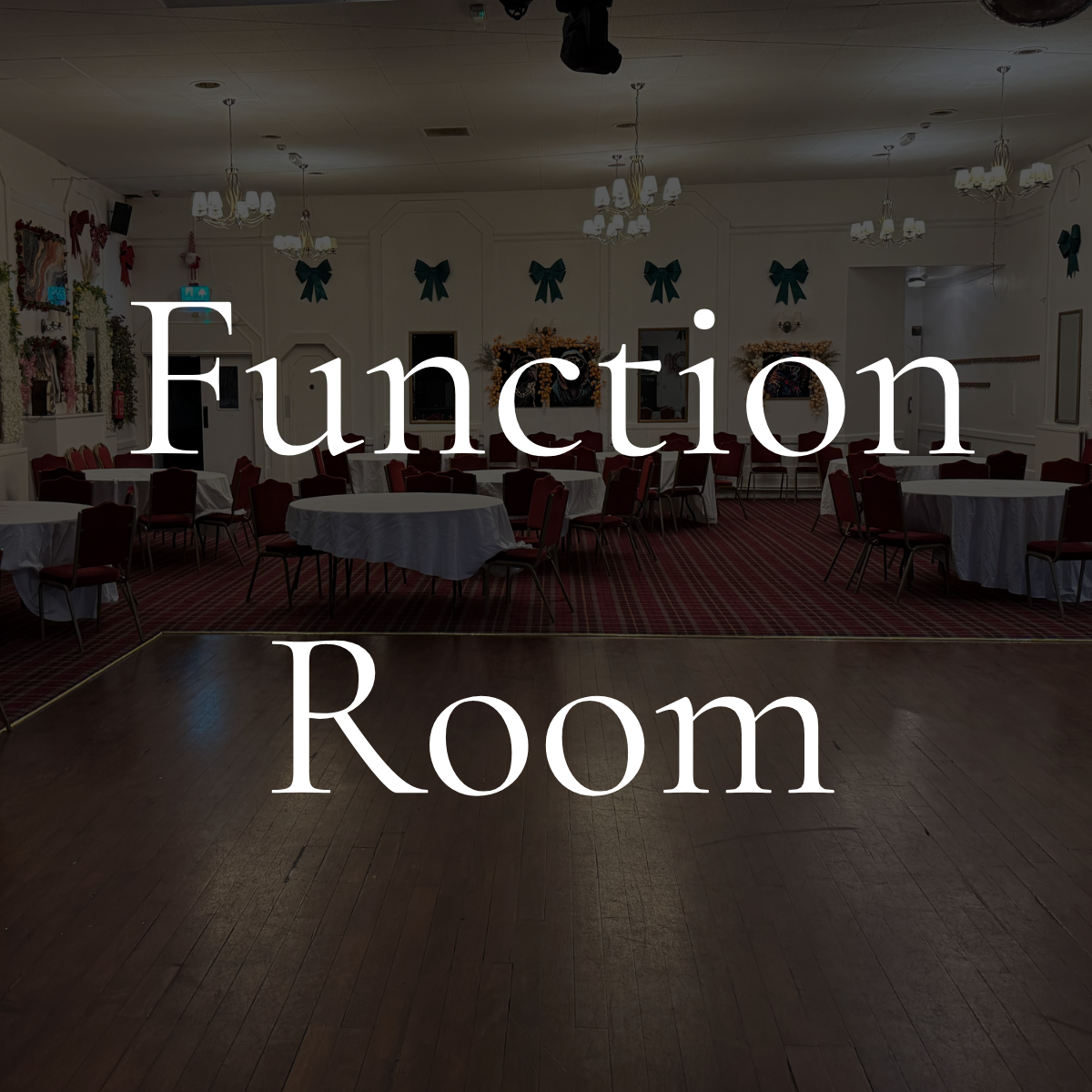 Empty banquet room decorated for a holiday event, with round tables covered in white tablecloths, chairs, chandeliers, and holiday wreaths with green bows on the walls.
