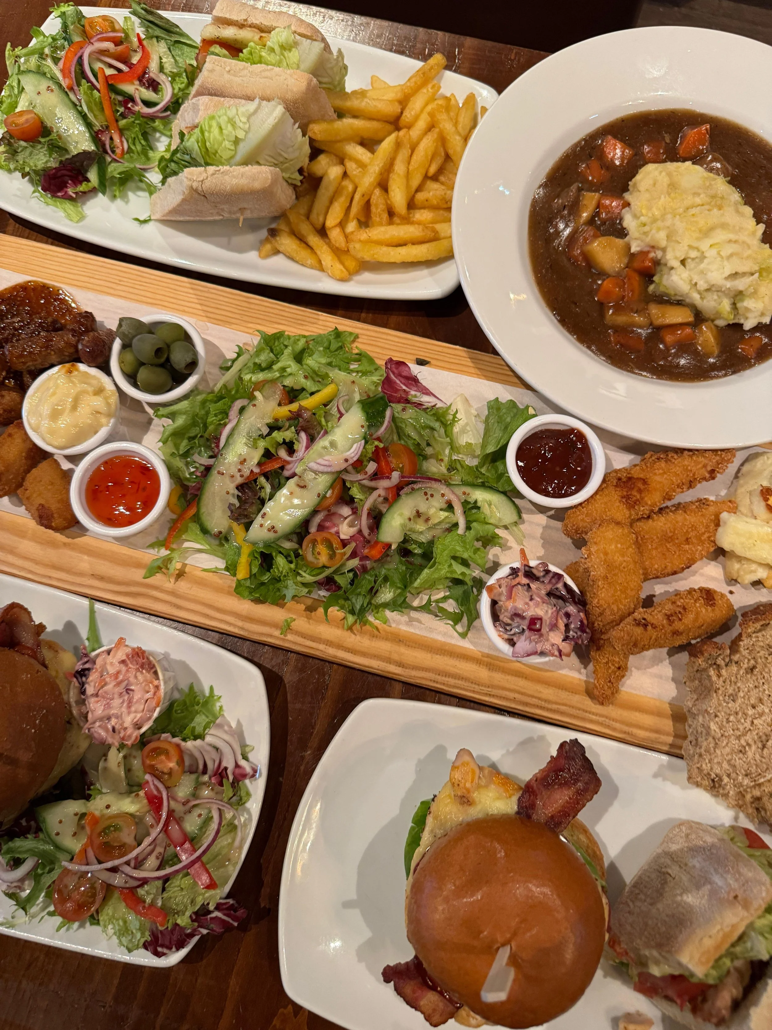 Assorted dishes including salads, sandwiches, fries, roasted meats, fried fish, a bowl of beef stew with mashed potatoes, and a burger.