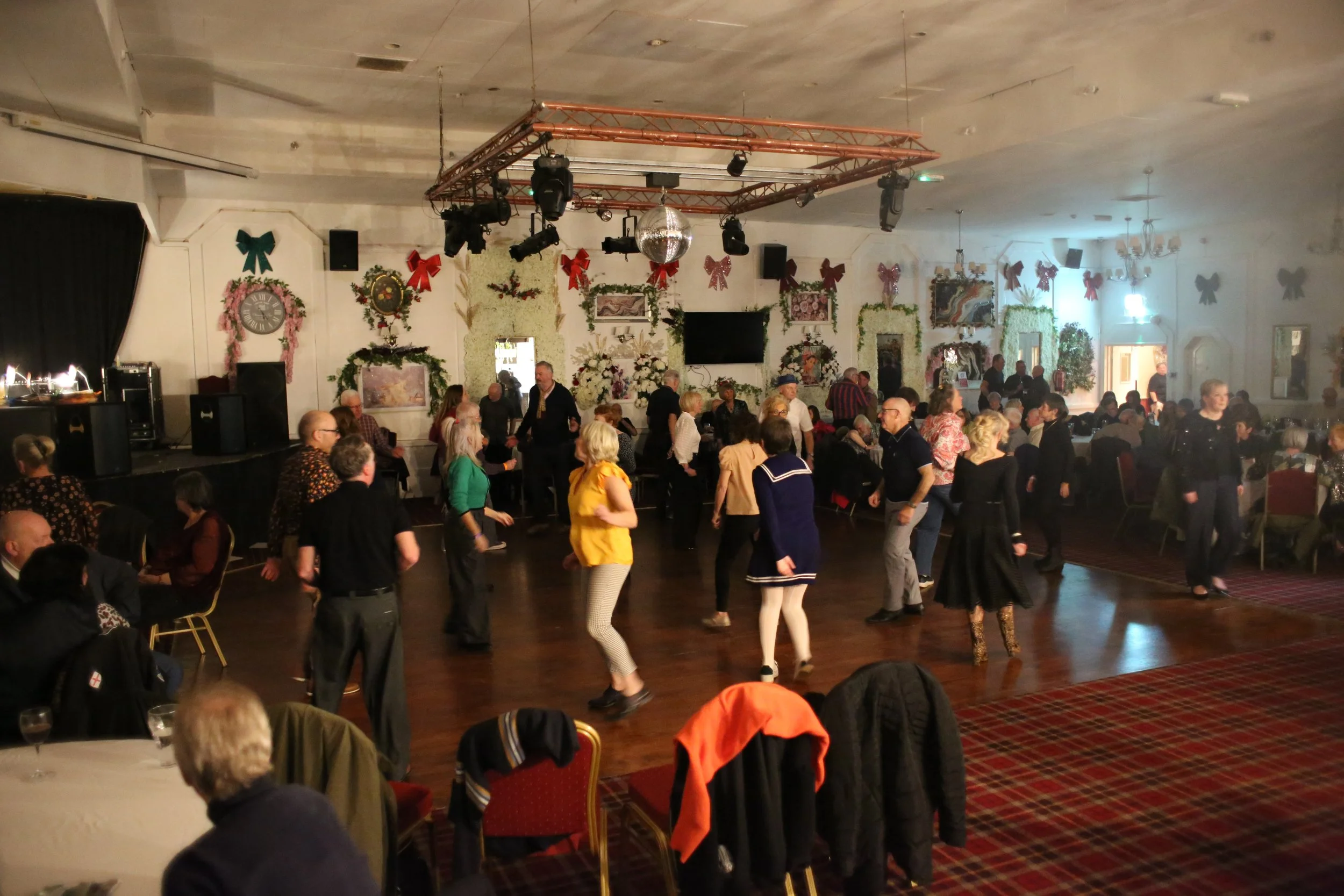 People dancing in a decorated banquet hall with holiday decorations and wall art.