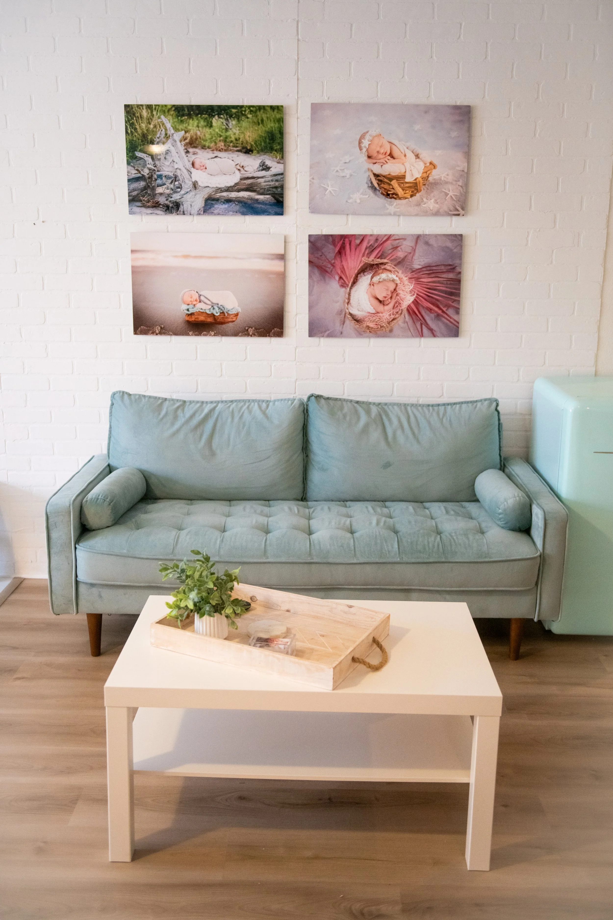 Living room with a light green sofa, white coffee table with a tray and potted plant, white brick wall with spring-themed baby photos, and a light blue side cabinet.