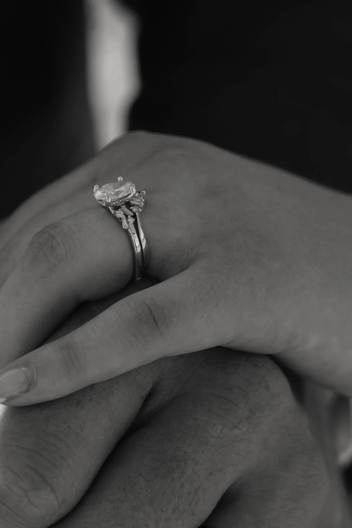 Close-up of a hand with a diamond engagement ring on the ring finger, in black and white.