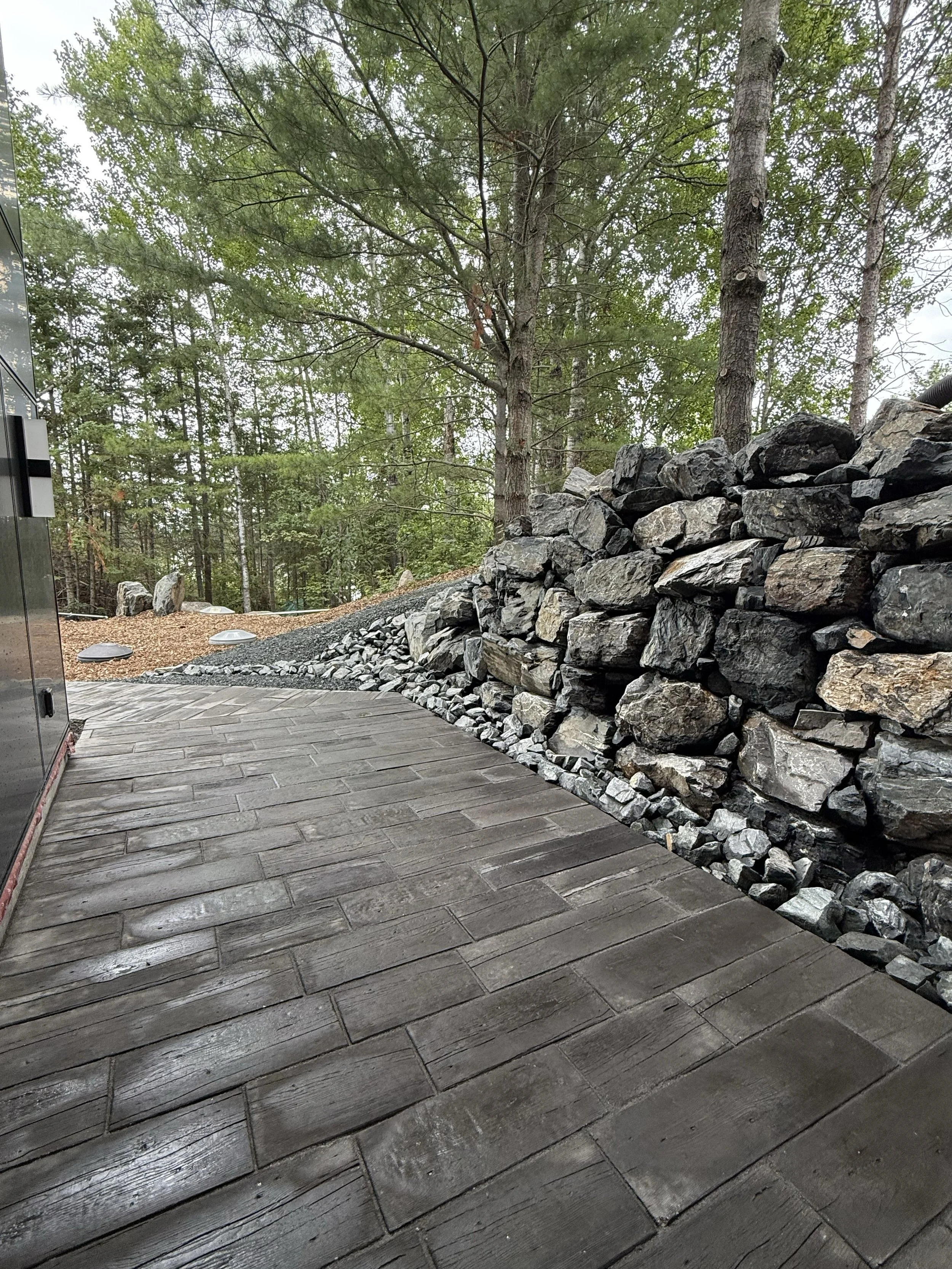 A wooden deck next to a constructed stone retaining wall with a forested background.