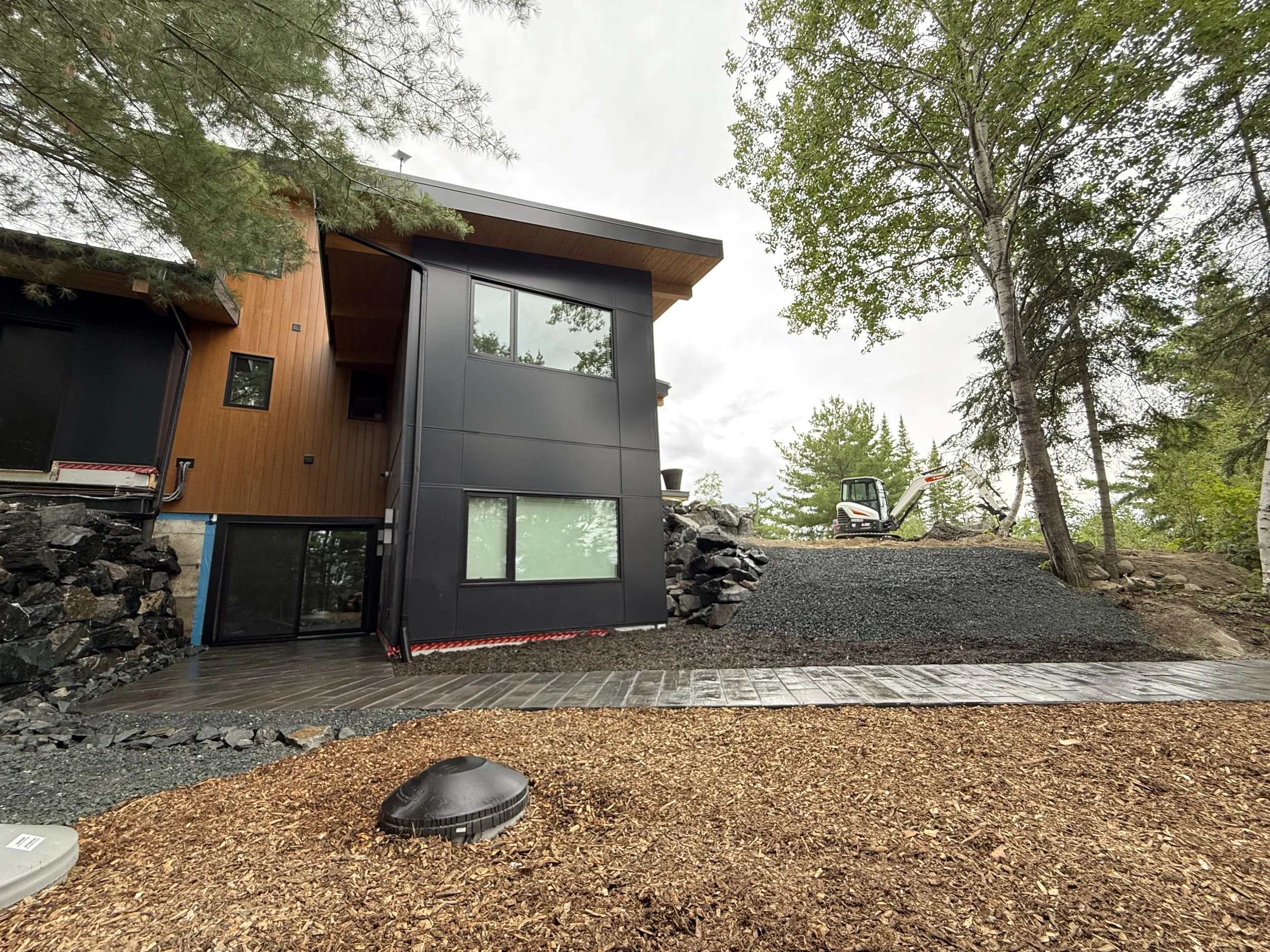 Modern house under construction with a yards and trees, construction equipment in the background.