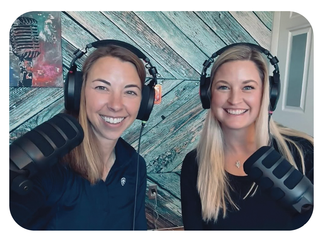 Two women with long hair wearing headphones and speaking into microphones in a podcast studio with a wood-paneled wall background.