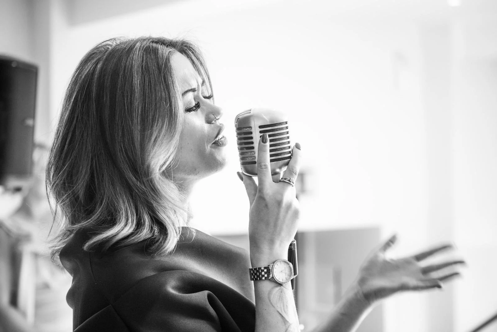 A woman with shoulder-length wavy hair singing into a vintage microphone, with her eyes closed and one hand raised, in black and white.