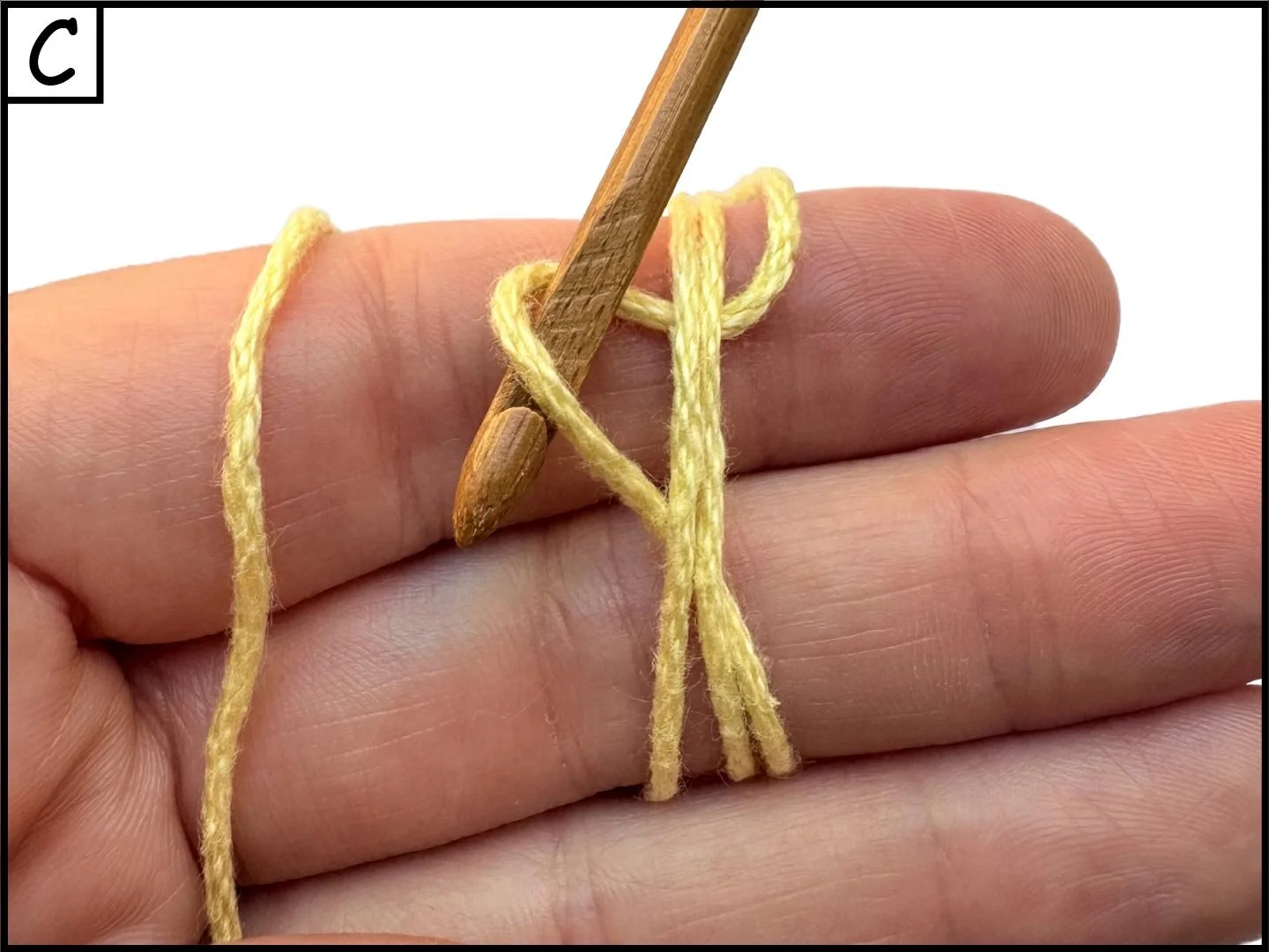 A person using a small wooden crochet hook to crochet with yellow yarn on their finger.