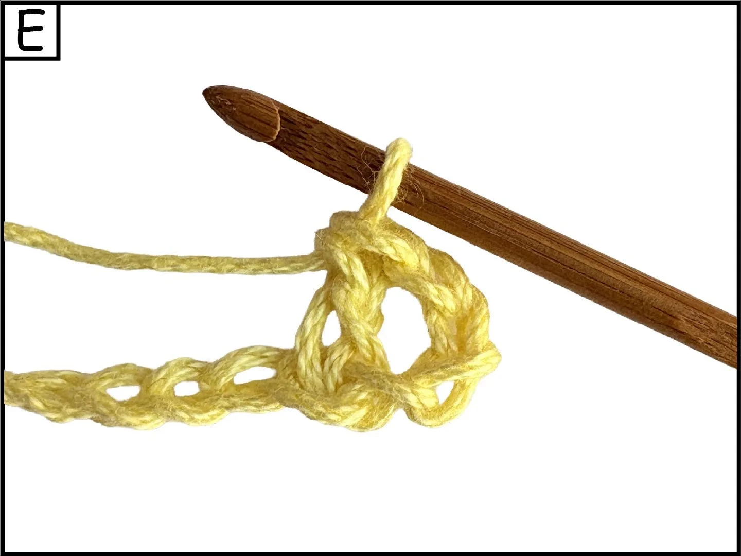 A wooden crochet hook piercing through a loop of yellow yarn, with some of the yarn looped and knotted.