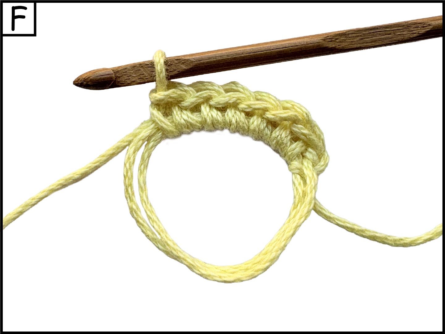 A close-up view of a wooden crochet hook piercing through a loop of yellow yarn, with some yarn looped around the hook, showing the process of crochet.