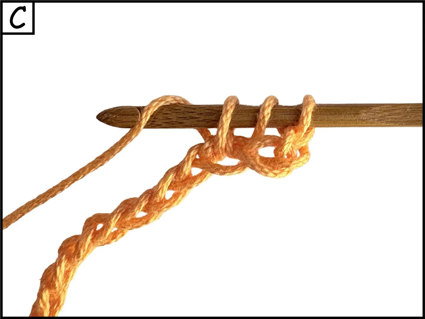A wooden crochet hook with orange yarn tied in a knot around it, held against a white background.