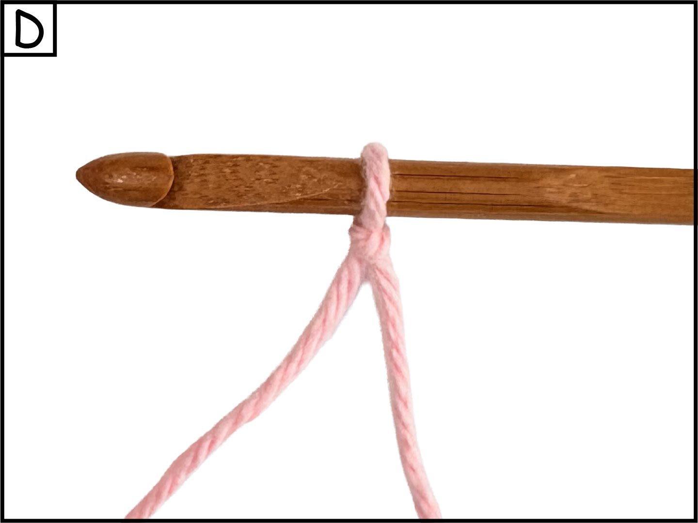 A wooden crochet hook with pink yarn looped around its top, isolated on a white background.