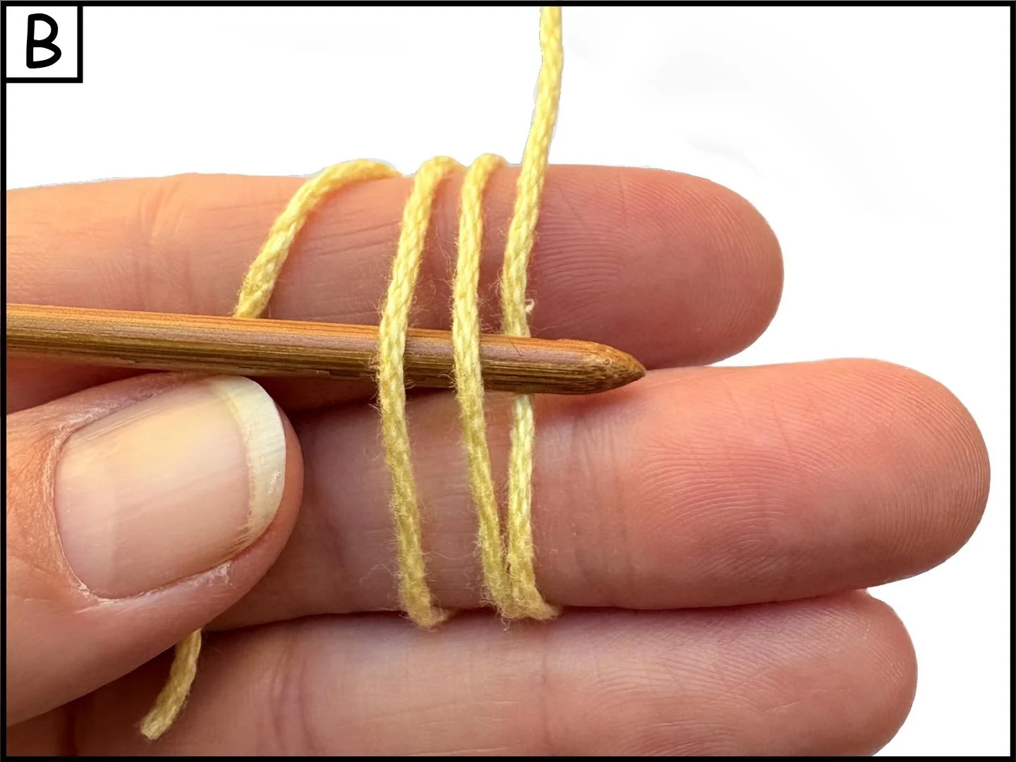 Close-up of a person's hand holding a wooden knitting needle with yellow yarn wrapped around fingers, preparing to knit.