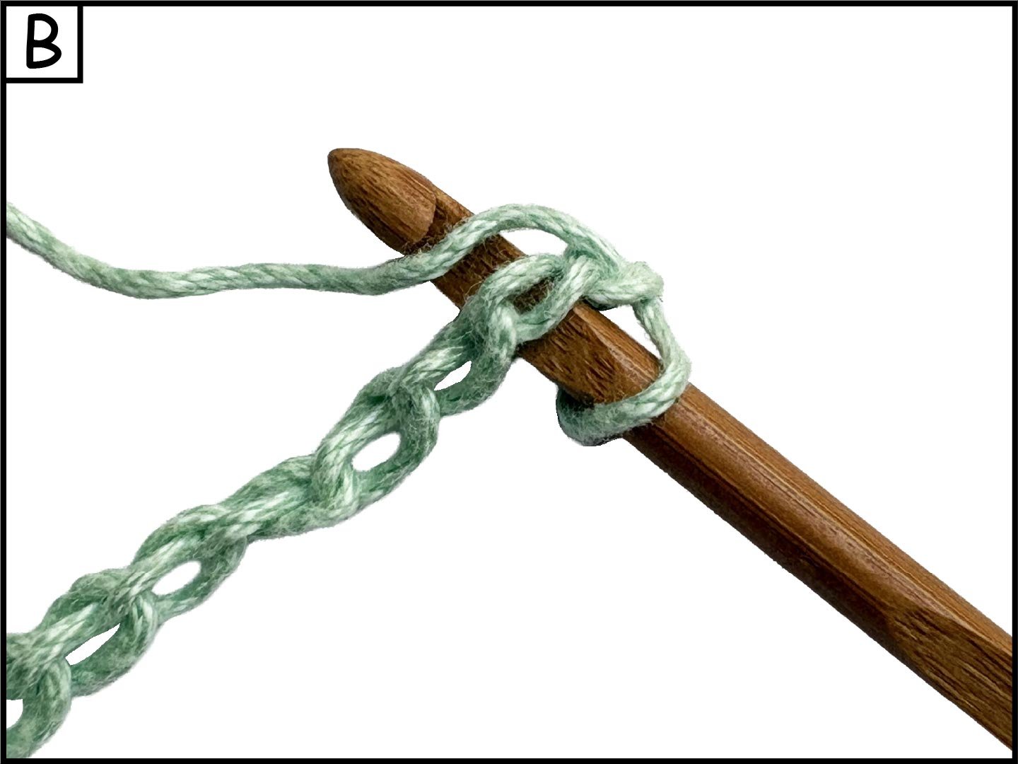 A wooden knitting needle with a green yarn thread tied in a knot around it, creating a loop in the yarn.