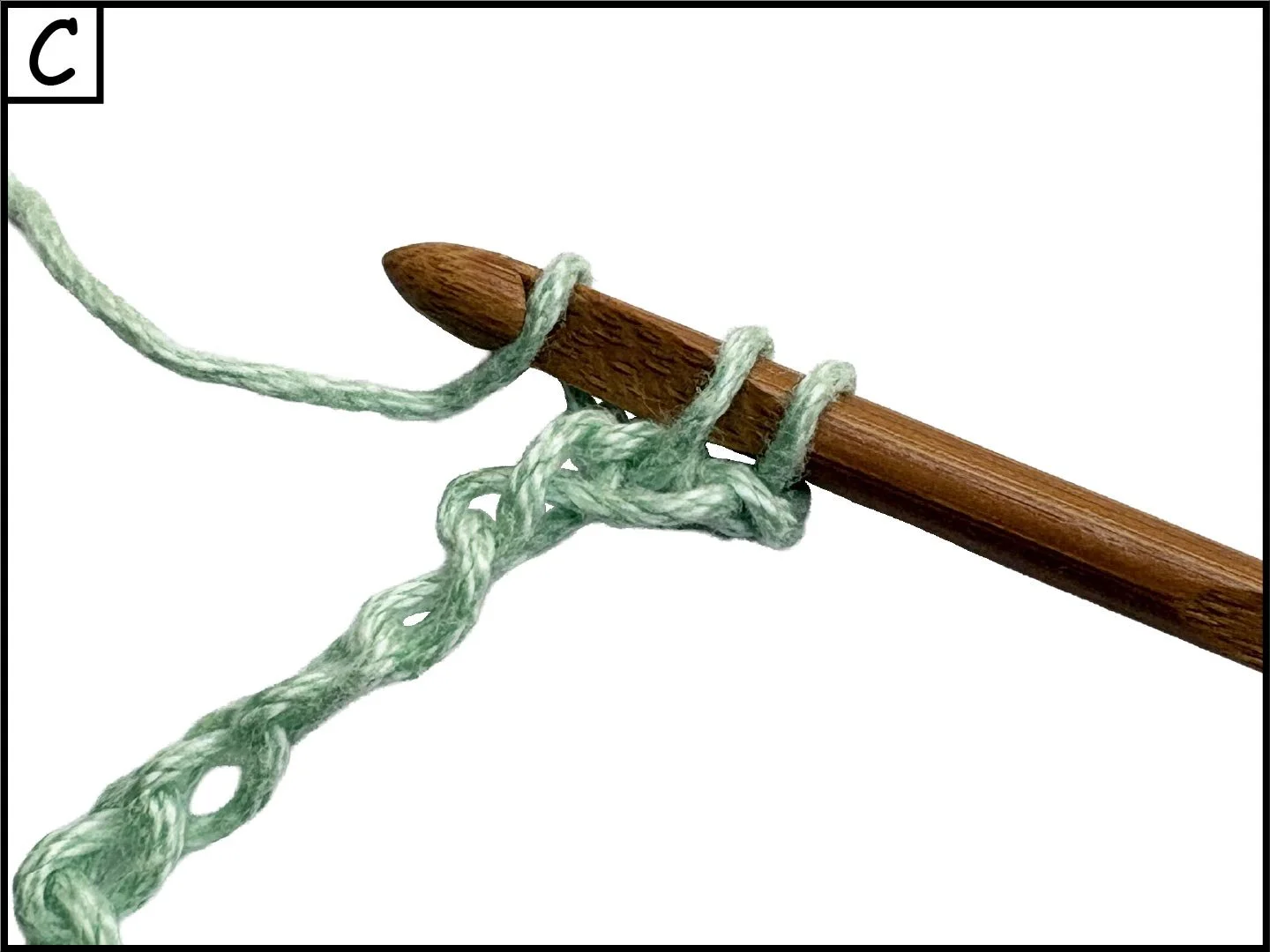 A wooden crochet hook with a green yarn looped around it.