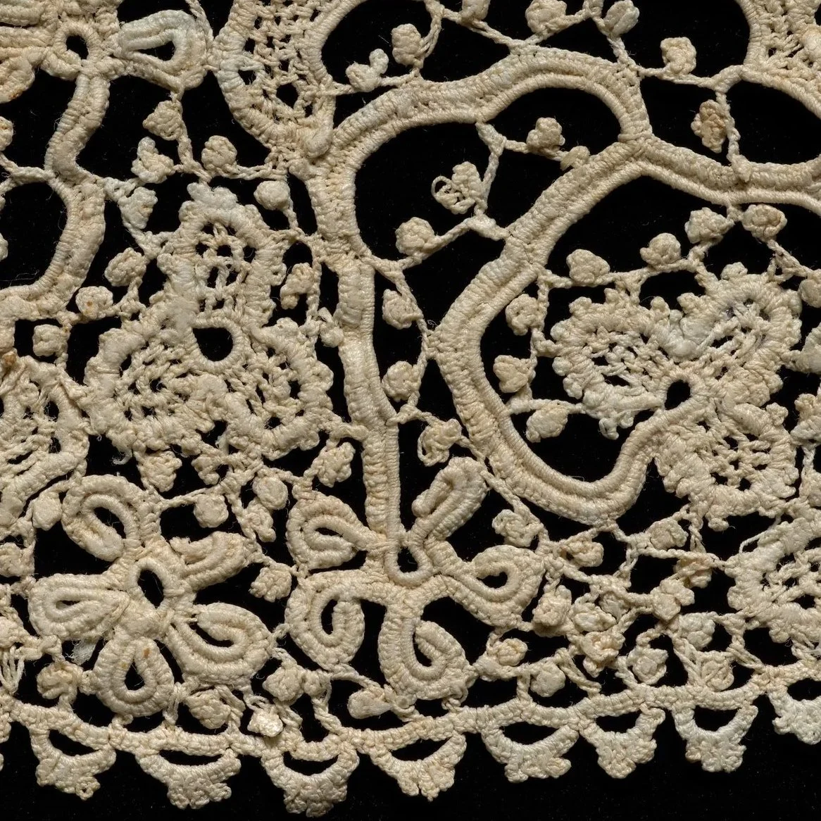 Close-up of white crochet lace fabric with floral and scroll patterns.