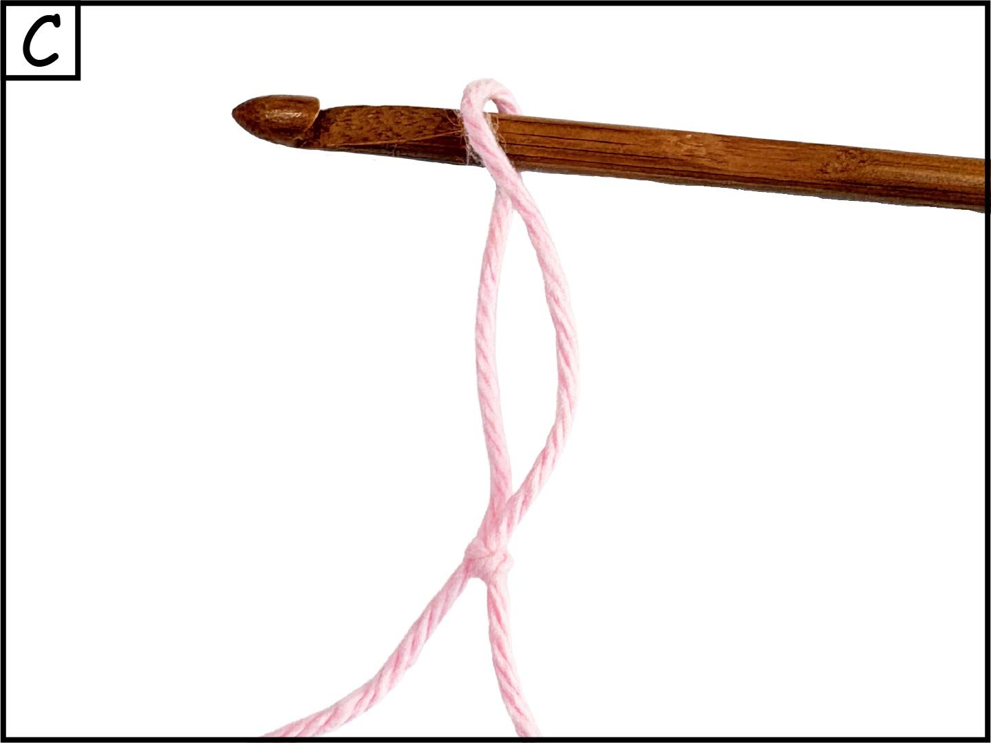 Pink yarn tied in a knot hanging from a wooden stick, against a white background.