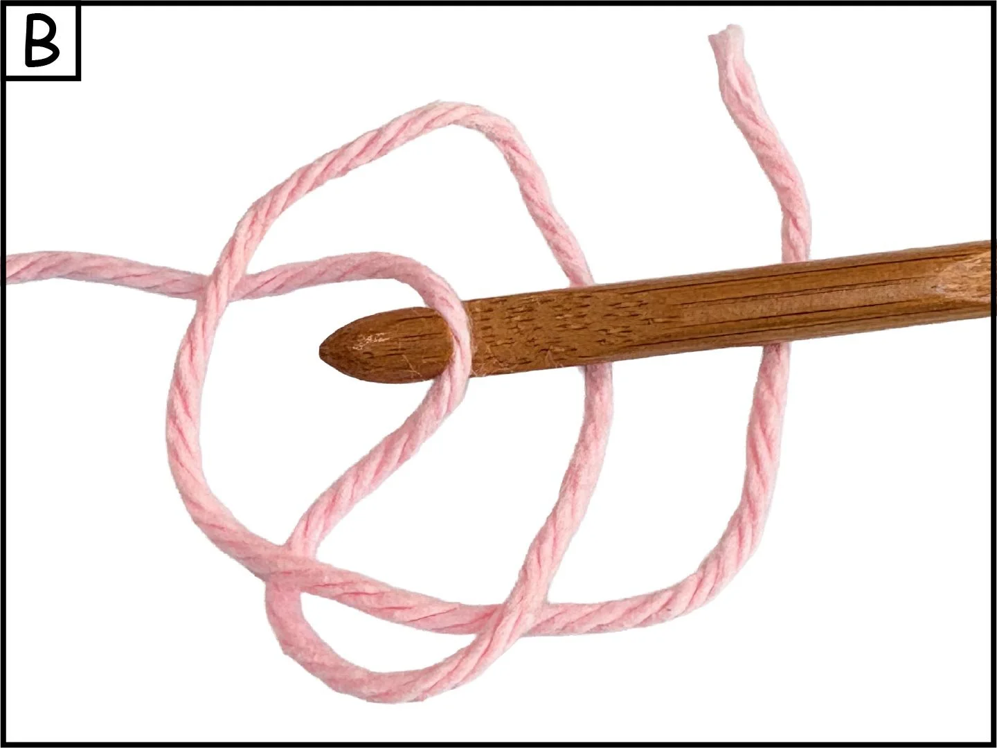 A wooden knitting needle with pink yarn looped around it against a white background.
