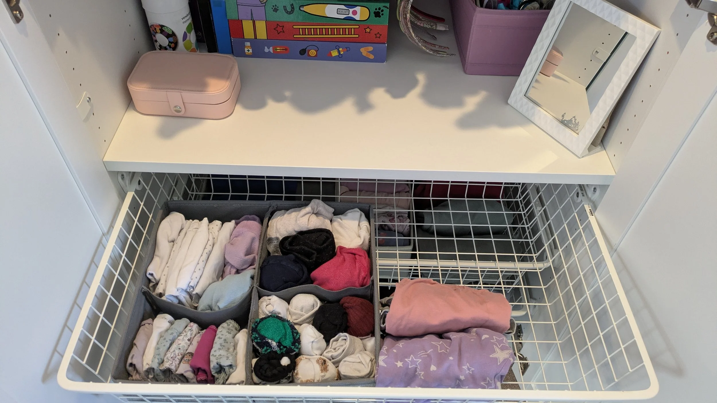 Open drawer with neatly folded socks and clothing, and organized storage bins on a white shelf above.