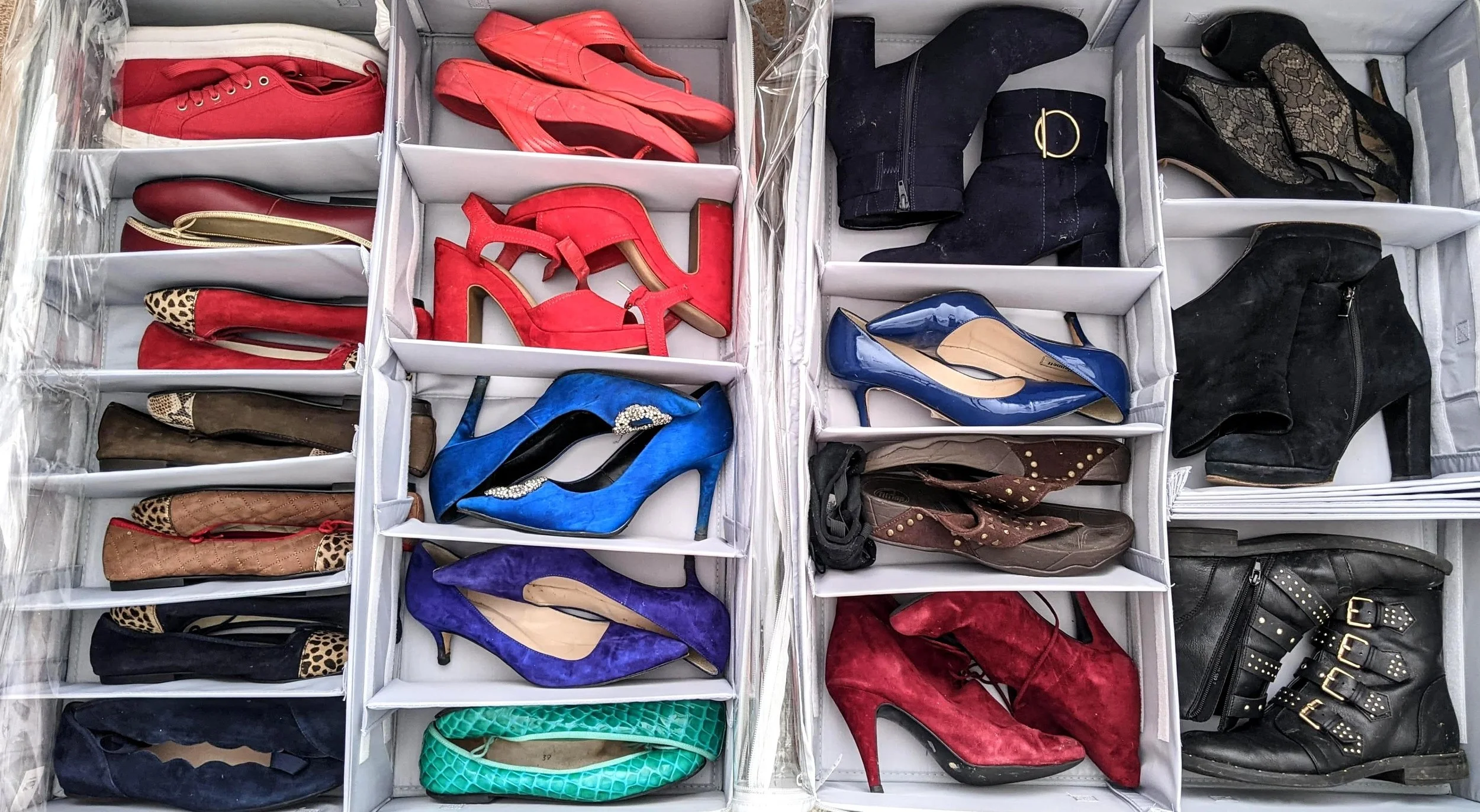 A large collection of shoes organized in a white multi-compartment storage container, including red shoes, blue high heels, black boots, leopard print shoes, and brown shoes.