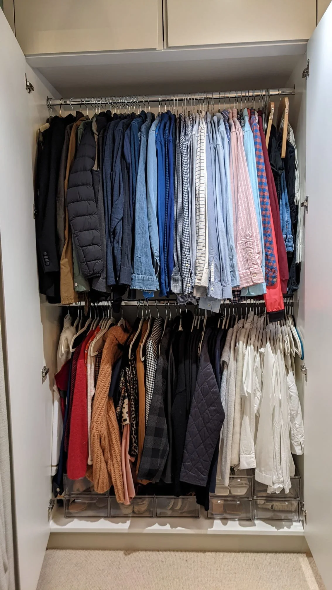 Closet with two shelves of hanging clothes, including jackets, shirts, sweaters, and pants in various colors and styles.