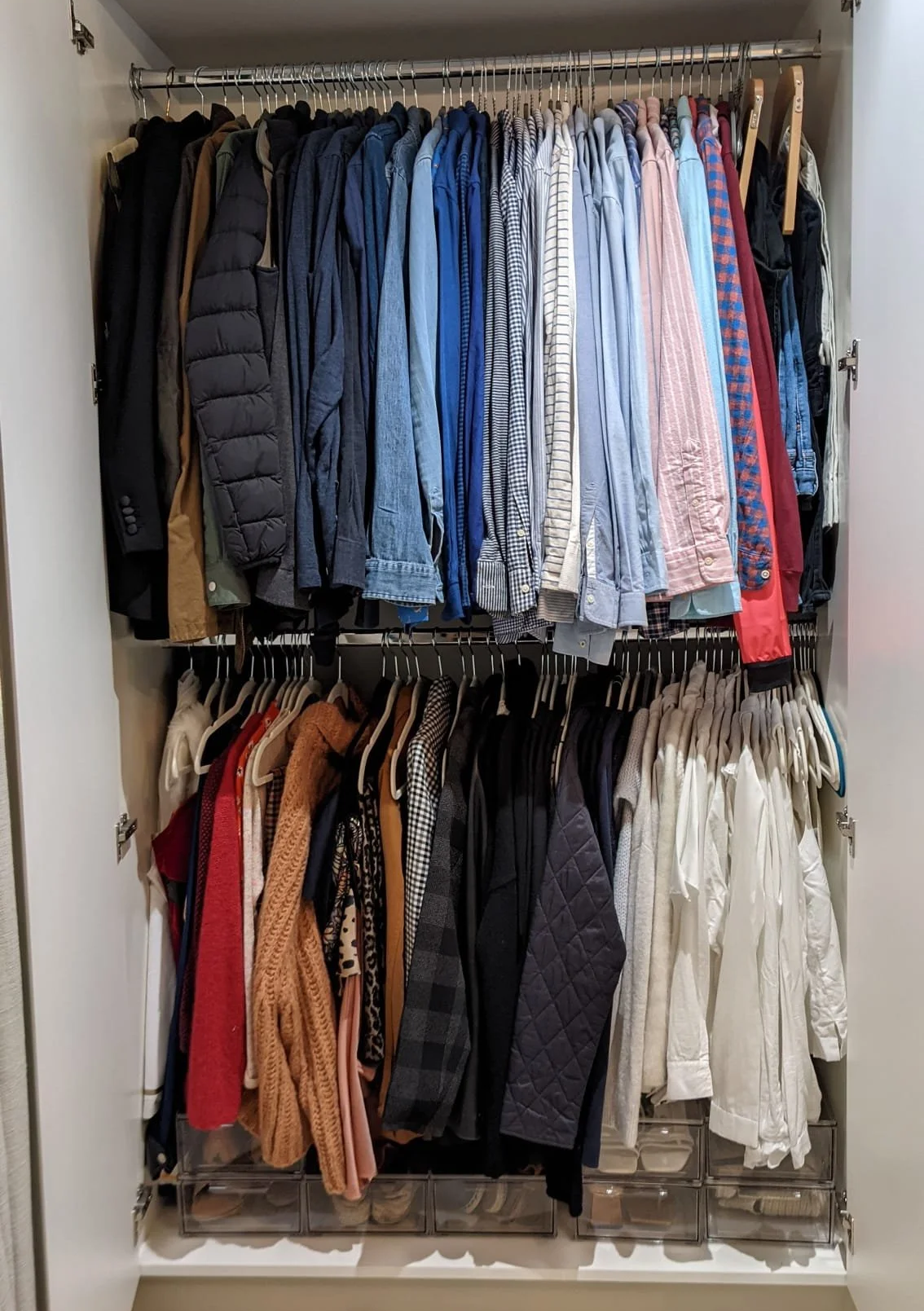 Open closet with two rows of hanging clothes, includes jackets, shirts, and sweaters, with clear plastic storage drawers at the bottom.