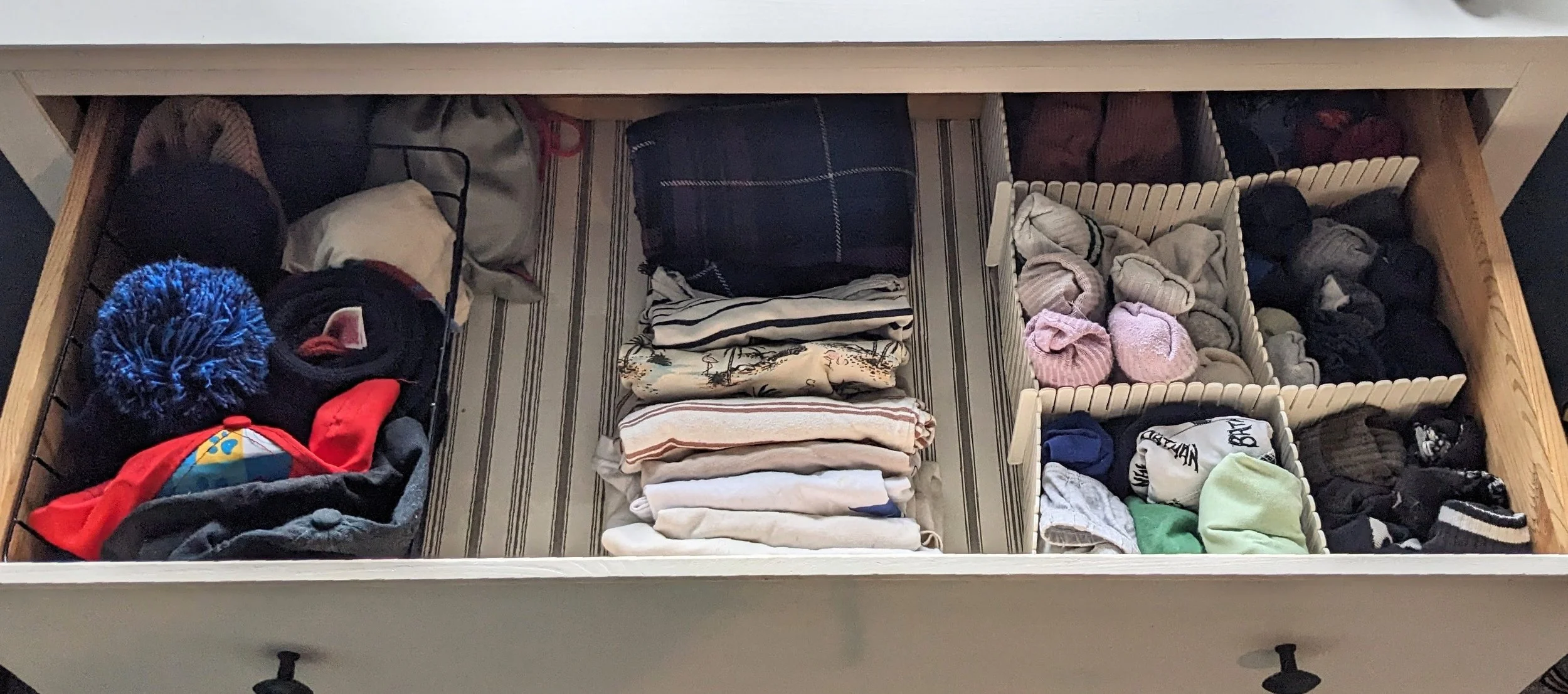Open drawer with organized clothing and accessories, including hats, scarves, folded T-shirts, socks, and underwear.