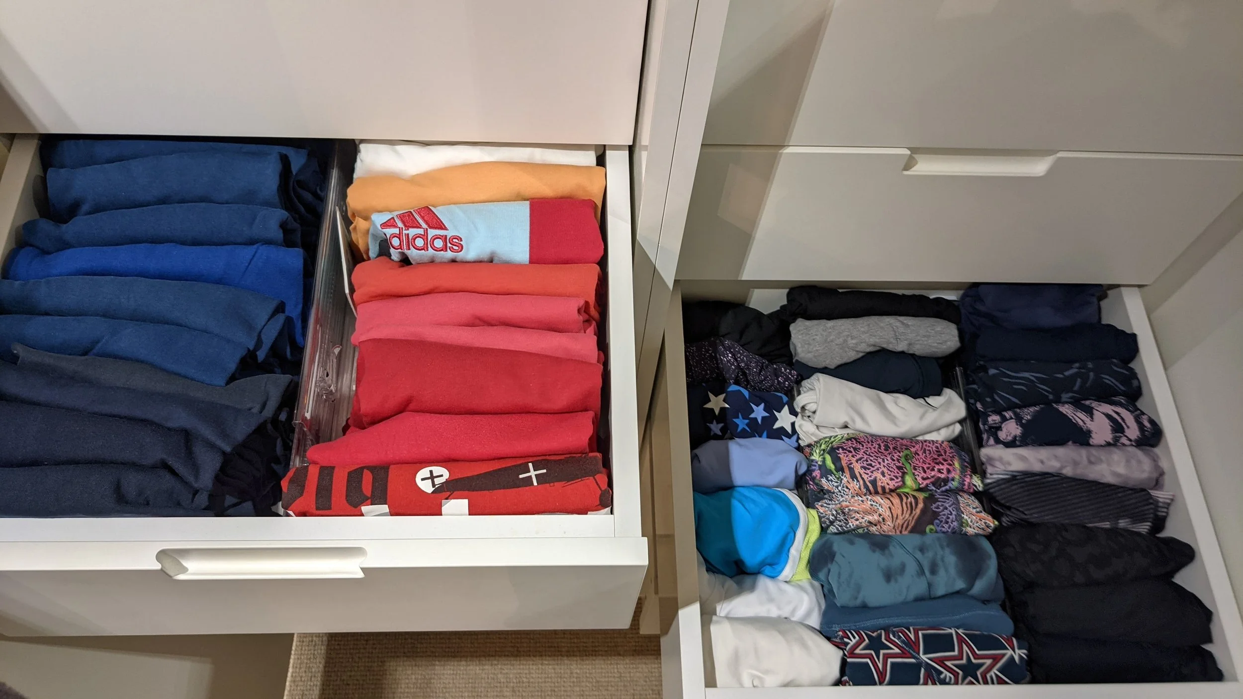 Open drawer with folded clothing, including colorful t-shirts on the left and various patterned and solid-colored clothing items on the right.